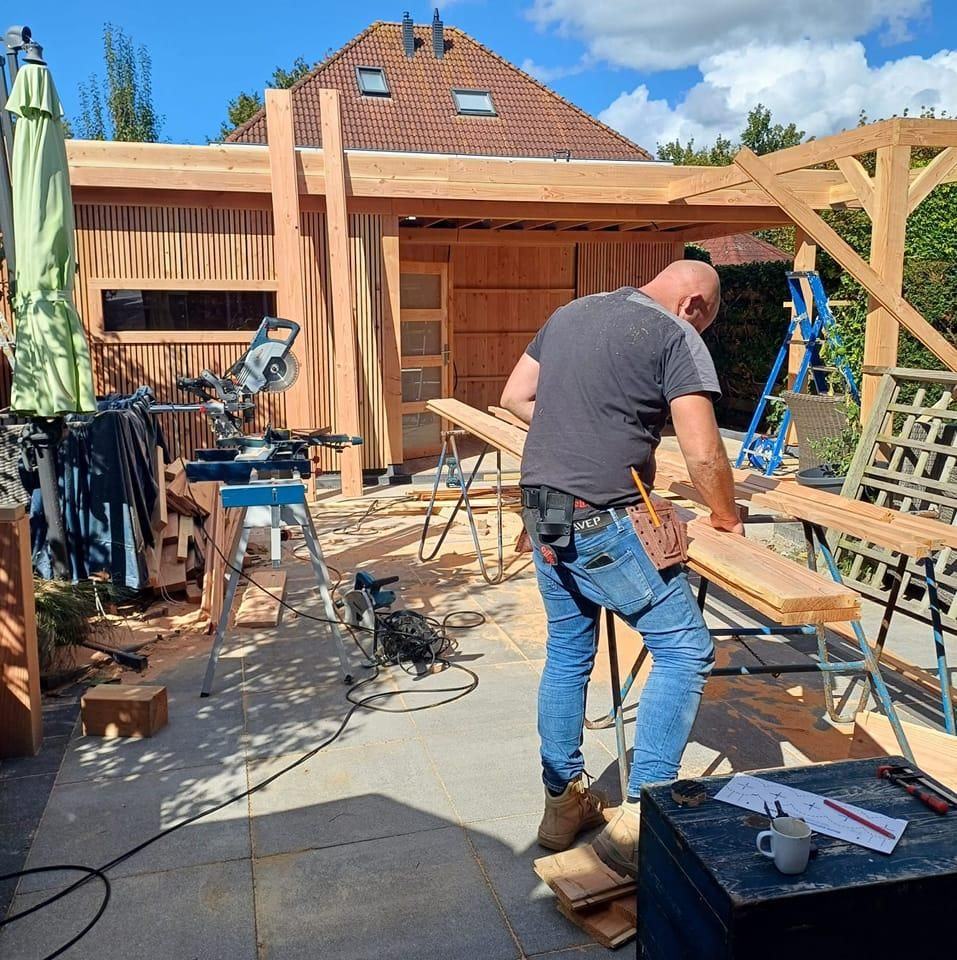 Bert-Jan aan het werk bij de afkortzaag, met een overkapping in aanbouw op de achtergrond