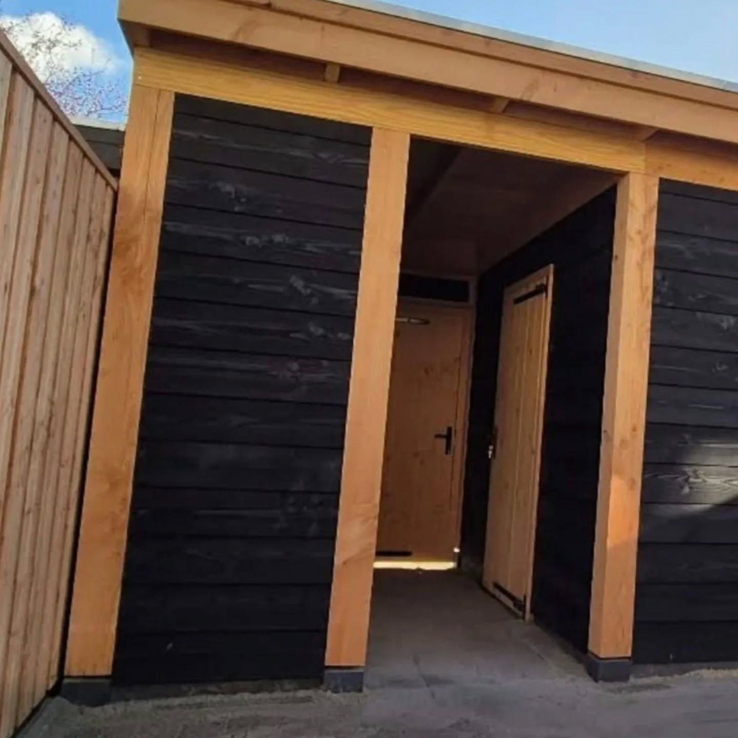 Zwart gebeitste schuur met een open Douglas overkapping